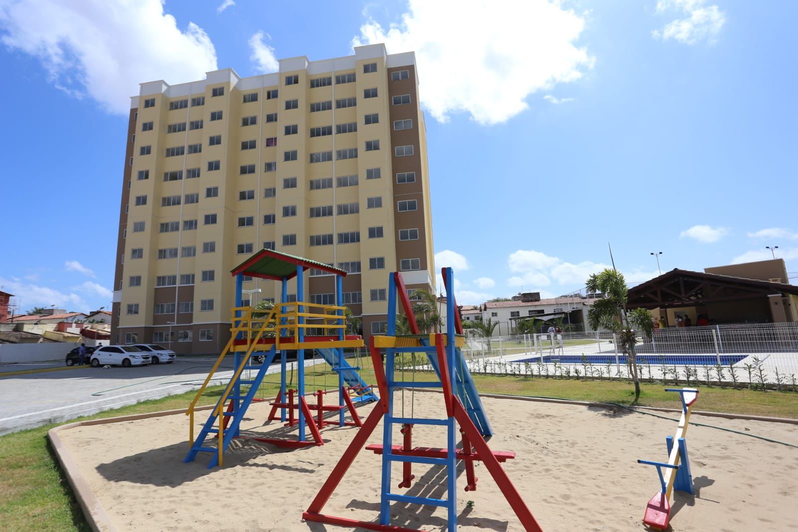 a foto mostra um playground com balanço e escorregador e, ao fundo, o prédio que foi contruídos